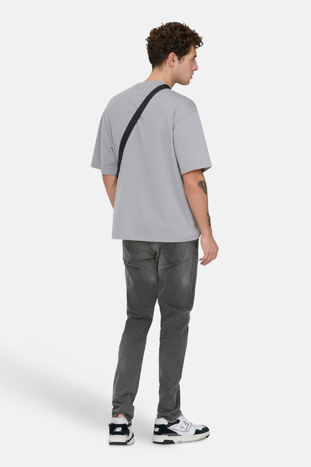 Donkergrijze slim jeans van ONLY & SONS, met subtiele wassing en gecombineerd met een grijs T-shirt en zwart tasje.