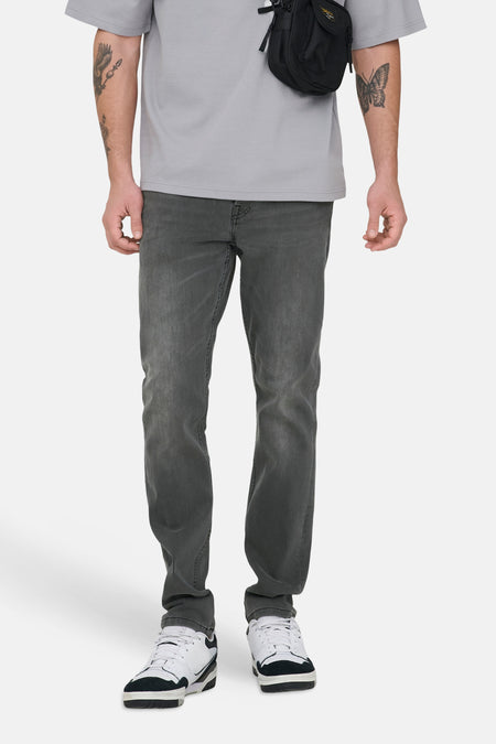 Donkergrijze slim fit jeans van ONLY & SONS, met subtiele wassing en gecombineerd met een grijs T-shirt en schoudertas.