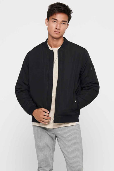 Veste noire d'ONLY & SONS®, à longues manches, portée sur un t-shirt beige avec des pantalons en denim gris et des baskets noires.
