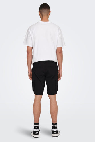 Achterkant man in witte T-shirt en zwarte cargo shorts, met zwarte en witte New Balance schoenen.
