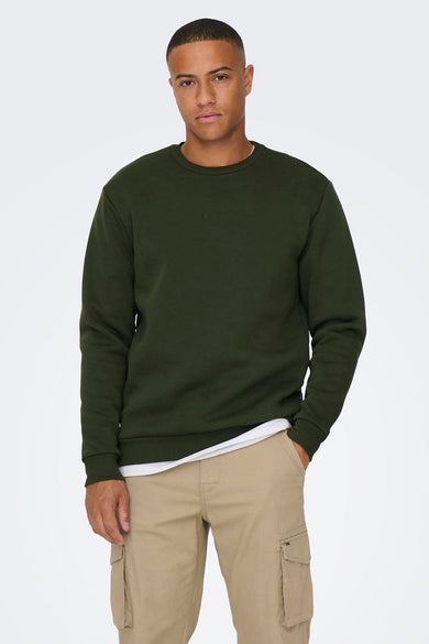 Pull-over vert en col rond de la marque ONLY & SONS®, porté avec un chemisier blanc et un pantalon cargo beige.