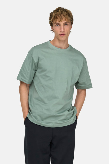 Groen T-shirt van ONLY & SONS®, gedragen met een zwarte broek, met de handen in de zakken.