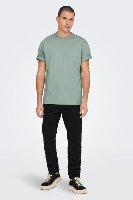 T-shirt vert de ONLY & SONS®, avec manches courtes repliées, porté avec un pantalon noir et des baskets chunky.