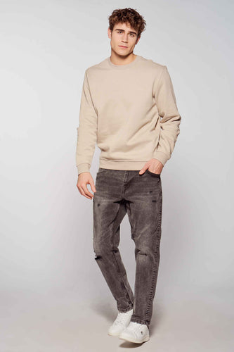 Man in beige sweater en grijze jeans.