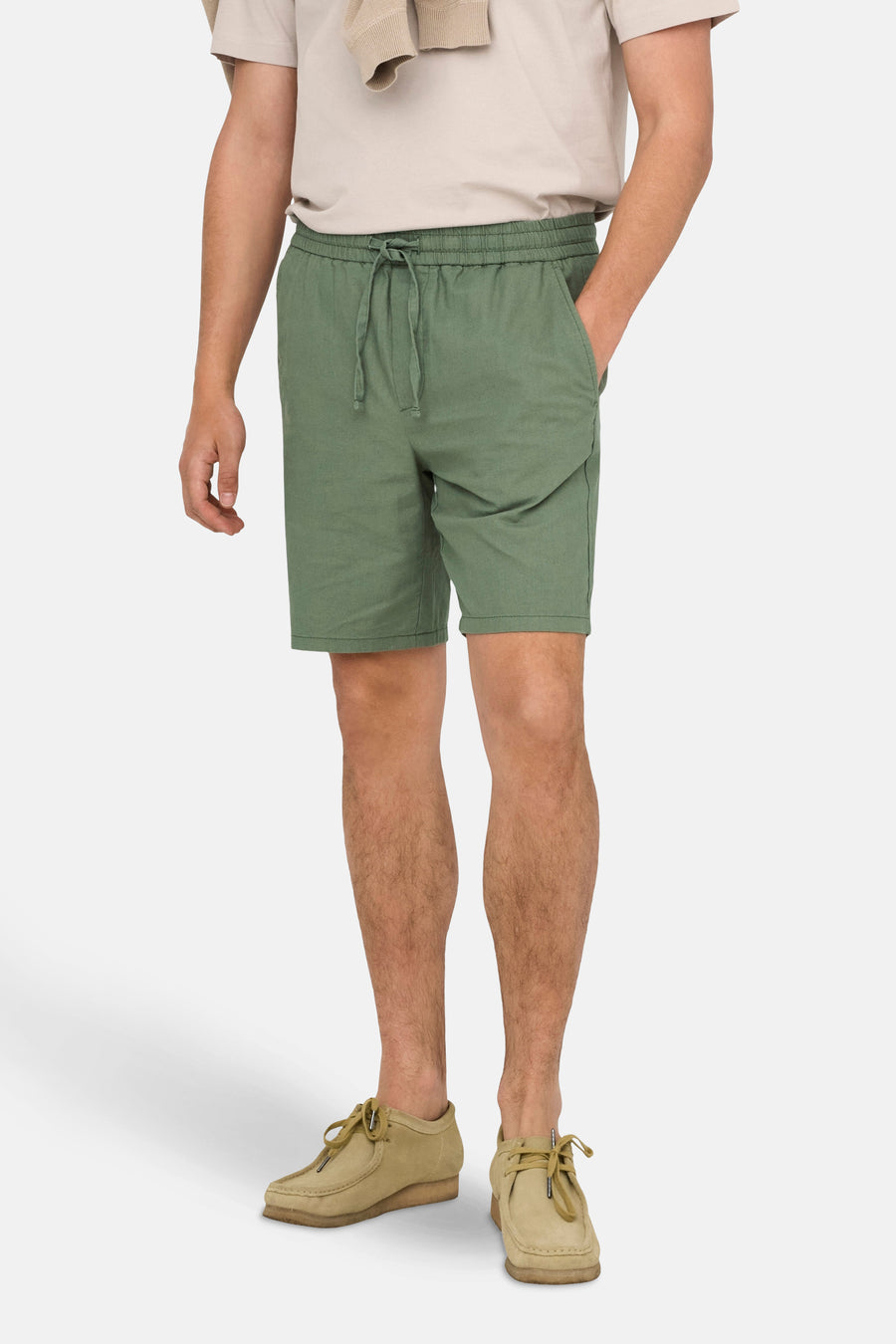 Staande man met groene shorts en beige schoenen.