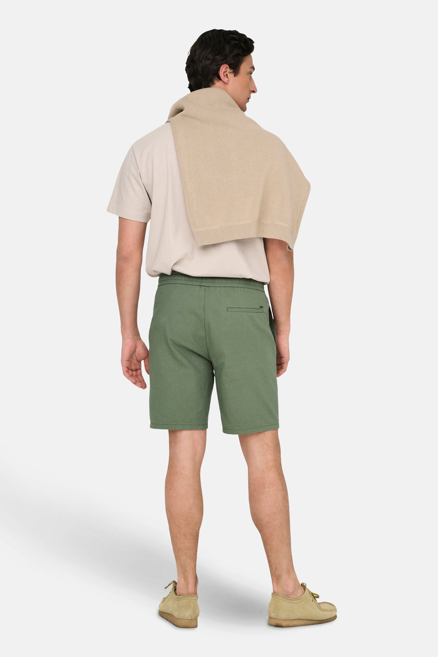 Man staat rug, kaki broek, beige shirt, suède schoenen.
