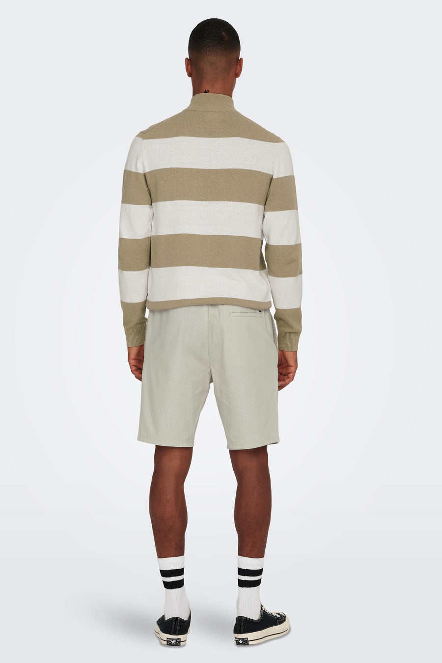 Man van achteren gezien, gestreepte trui, korte broek, sokken met strepen en sneakers.