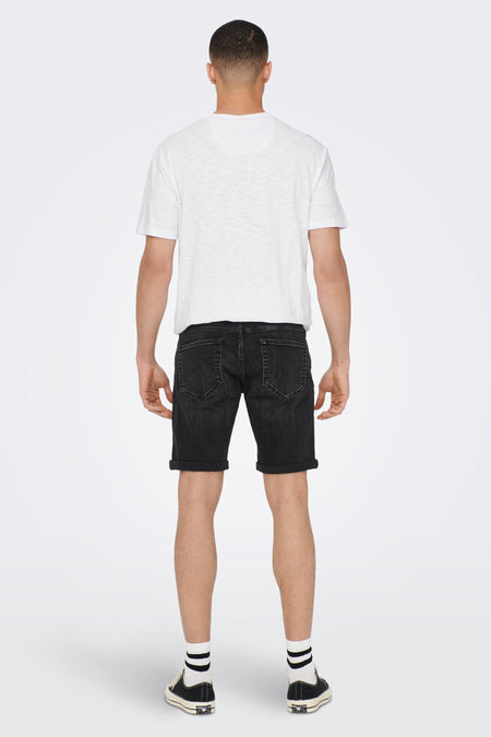 Zwarte denim jeansshort van ONLY & SONS, met opgerolde pijpen, gedragen met een wit T-shirt en zwarte sneakers met witte sokken, achteraanzicht.
