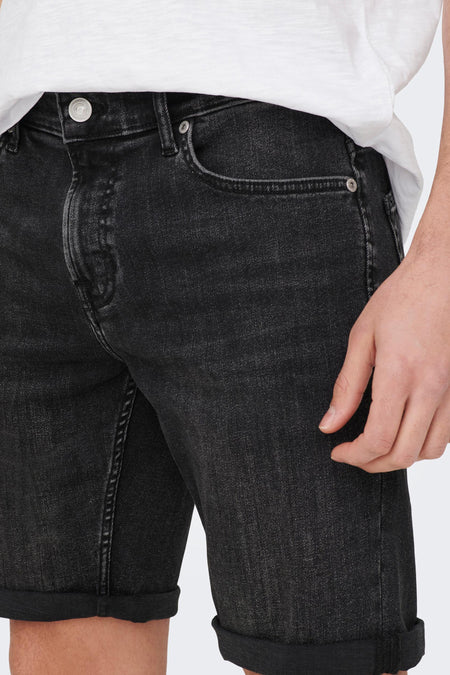 Zwarte denim jeansshort van ONLY & SONS, met omgeslagen pijpen en een hand in de buurt.
