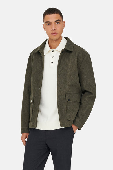 Manteau brun court de ONLY & SONS®, avec des poches et porté sur un chemisier blanc et un pantalon foncé.
