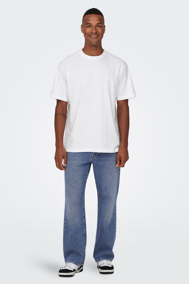 Jean en denim bleu large de ONLY & SONS®, avec des baskets blanches et un T-shirt blanc.