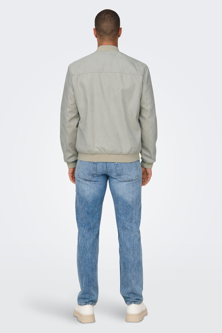 Man van achteren gezien, lichtgrijze jas, blauwe jeans, witte schoenen.
