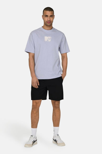 Short noir d'ONLY & SONS, associé à un T-shirt bleu clair avec le logo MTV et des baskets blanches avec des détails noirs.