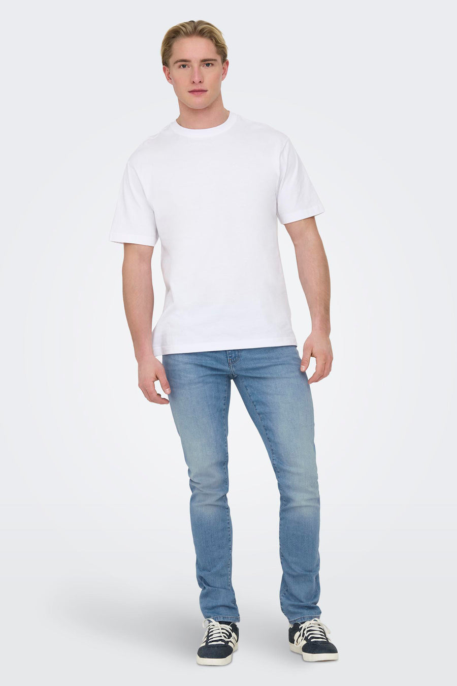 Jean slim en denim bleu clair de ONLY & SONS®, porté avec un T-shirt blanc et des baskets noires.