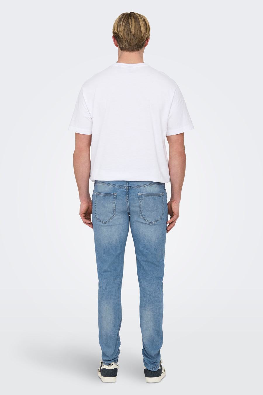 Jean slim fit en denim bleu clair de ONLY & SONS, vu de derrière, avec un T-shirt blanc et des baskets noires.