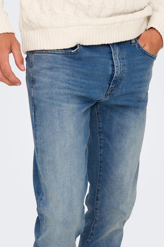 Jean droit bleu clair d'ONLY & SONS®, avec la main dans la poche, porté avec une chemise à col roulé blanche.