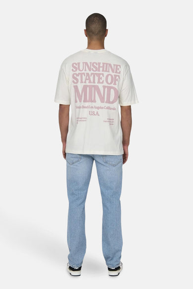 T-shirt beige à manches courtes de ONLY & SONS®, avec une impression rose et porté avec un jean bleu.