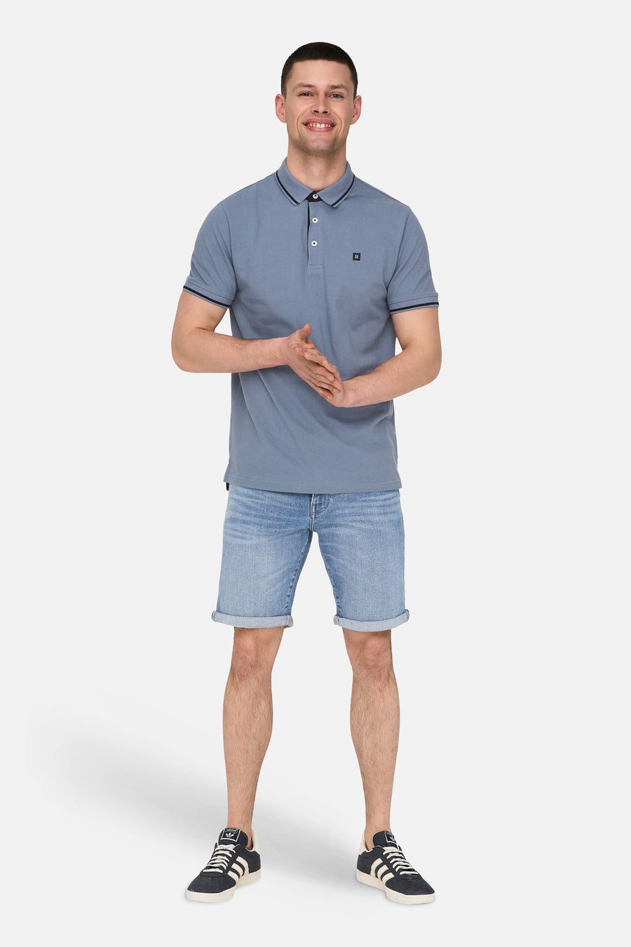 Mid blue denim jeansshort van ONLY & SONS, met opgerolde pijpen en gecombineerd met een blauw polo shirt en sneakers.
