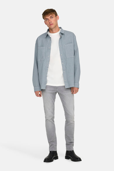 Chemise en denim bleu clair à manches longues de ONLY & SONS, portée sur un T-shirt blanc et des jeans gris avec des bottes noires.