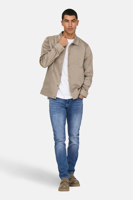 Man in beige jas, wit shirt, jeans en bruine schoenen.