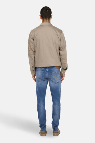 Achterkant van een man in een bruine jas, blauwe jeans en bruine schoenen.