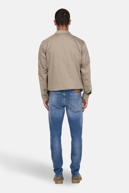 Achterkant van een man in een bruine jas, blauwe jeans en bruine schoenen.