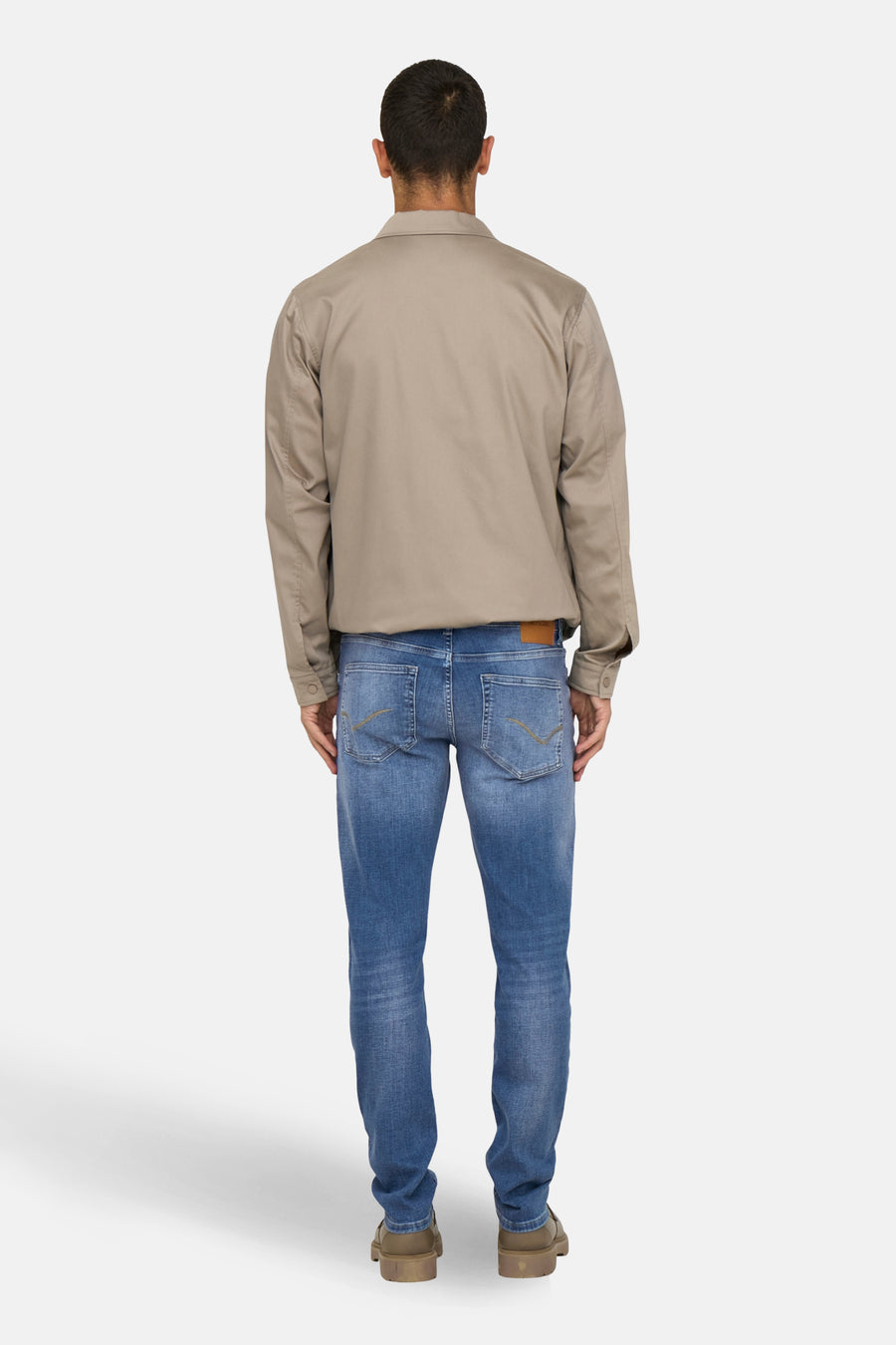 Achterkant van een man in een bruine jas, blauwe jeans en bruine schoenen.