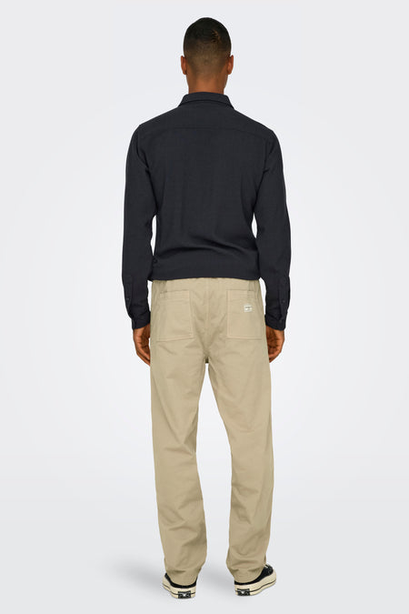 Beige broek van ONLY & SONS® met achterzakken, gecombineerd met een zwart overhemd en zwarte schoenen.
