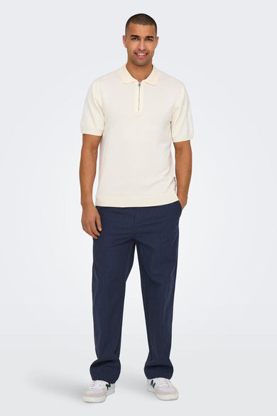 Pantalon bleu d'ONLY & SONS avec une rayure blanche et un ajustement décontracté, associé à un poloshirt crème avec des manches courtes et un zip.