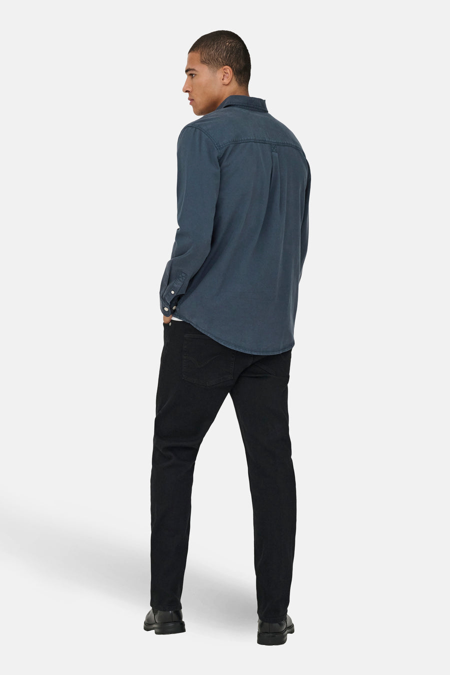 Een man van achteren gezien, in een blauw overhemd en zwarte broek.