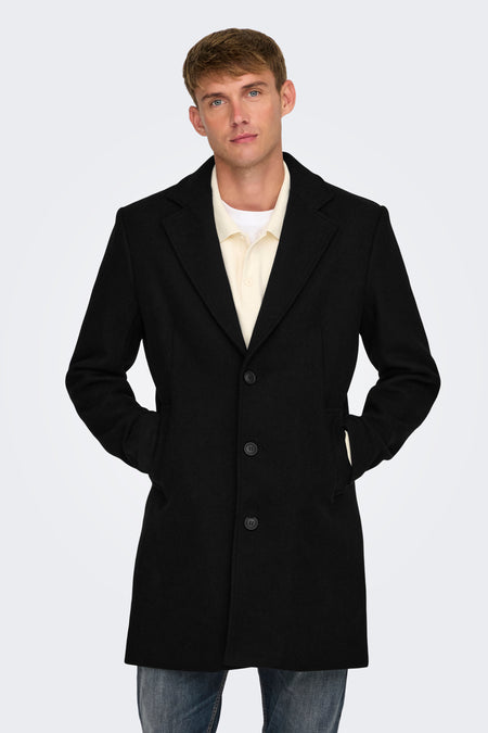 Veste longue noire d'ONLY & SONS, à boutons et poches, portée sur un polo jaune et des pantalons de travail.