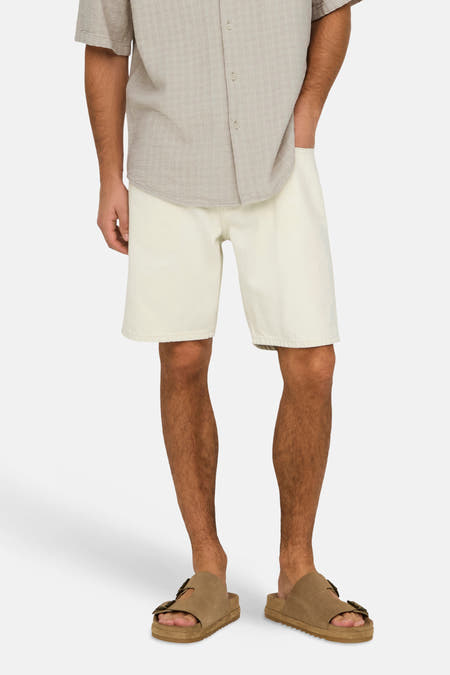 Short en jean écru de ONLY & SONS®, combiné avec une chemise beige et des sandales marron.