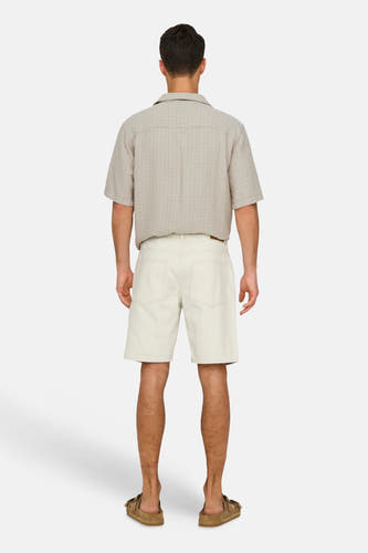 Short en jean écru de ONLY & SONS, vu de dos, combiné avec une chemise beige et des sandales marron.