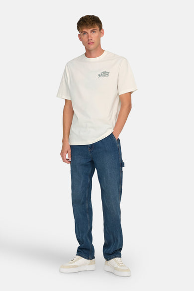 T-shirt écru à manches courtes de ONLY & SONS®, avec une petite impression textuelle et associé à des jeans bleus et des baskets crème.