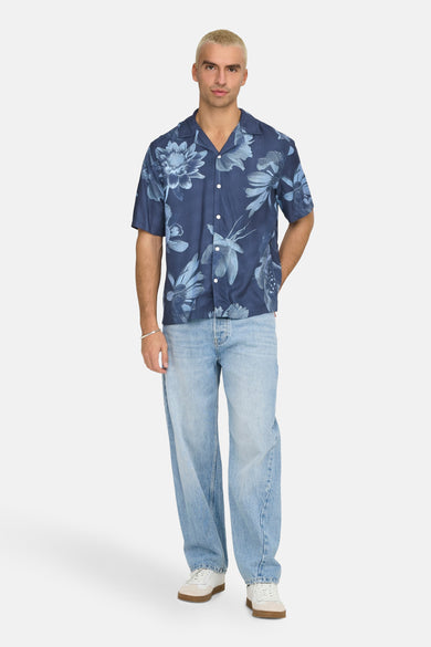 Chemise bleue à manches courtes de ONLY & SONS, avec un motif floral, portée avec des jeans décontractés et des baskets blanches.