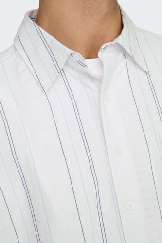 Chemise blanche à manches longues de ONLY & SONS®, motif rayé et col boutonné, portée sur une chemise blanche.