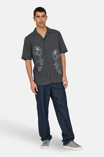 Chemise grise à manches courtes de ONLY & SONS, avec des motifs floraux blancs et portée avec des jeans bleus marine et des baskets grises.