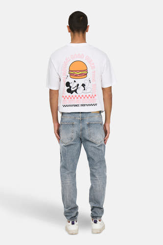 Jean tapered bleu clair de ONLY & SONS, avec une finition stonewash, associé à un T-shirt blanc avec imprimé Mickey Mouse et des baskets blanches.
