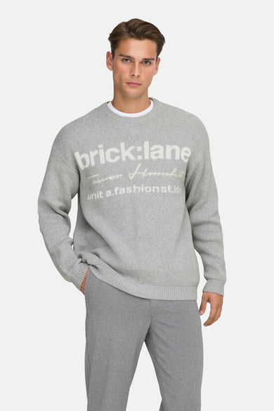 Sweat gris à col rond de ONLY & SONS®, avec un imprimé, porté sur une chemise blanche, associé à un pantalon gris.
