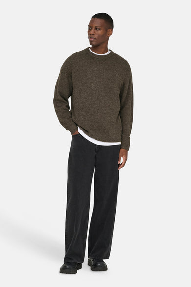 Een man in een groene trui en zwarte jeans, staand.