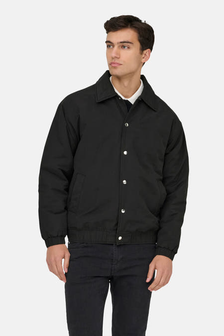 Veste noire d'ONLY & SONS, à longues manches, avec fermeture à boutons et poches, portée sur une chemise blanche, un pull noir et un jean noir.