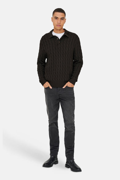 Bruine trui van ONLY & SONS, met kabelpatroon en gedragen over een wit T-shirt met grijze jeans en zwarte laarzen.
