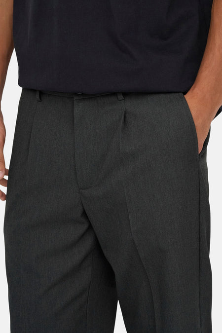 Grijze pantalon met plooien en hand in de zak.
