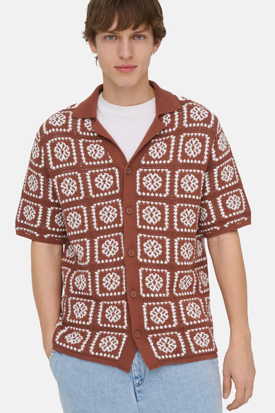 Pull en maille marron ONLY & SONS® avec motif carré blanc ressemblant à des flocons de neige, porté sur un t-shirt blanc et un jean clair.