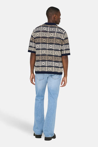 Pull multicolore à col en V de ONLY & SONS®, avec motif géométrique, manches courtes et porté avec un jean bleu clair et des chaussures noires.