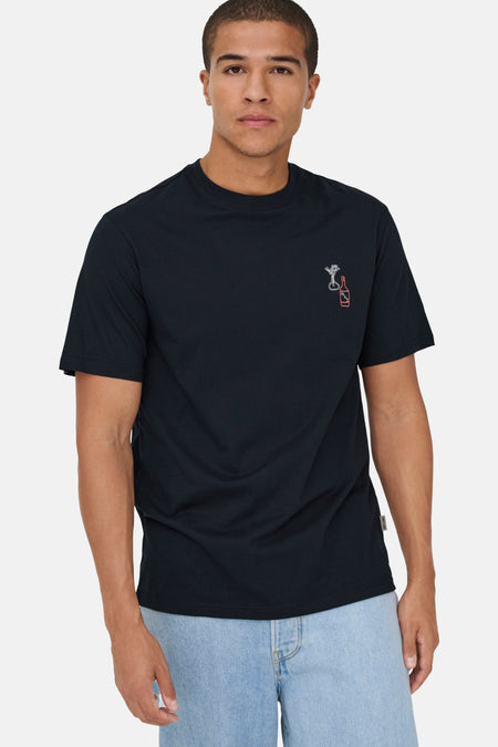 Man in zwart T-shirt met drankmotief en lichte jeans, staand tegen witte achtergrond.