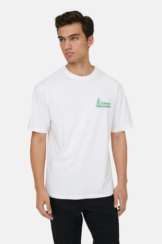 T-shirt blanc à manches courtes de ONLY & SONS®, avec une impression verte sur la poitrine et porté avec un pantalon noir.