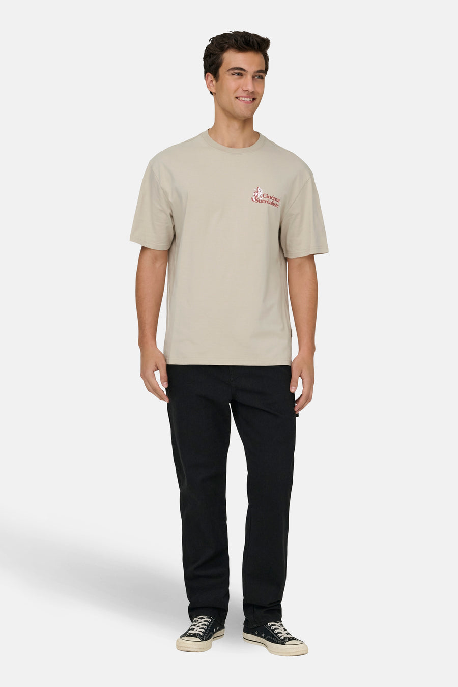 T-shirt écru à manches courtes de ONLY & SONS®, avec une impression rouge sur la poitrine, associé à un pantalon noir et des chaussures.