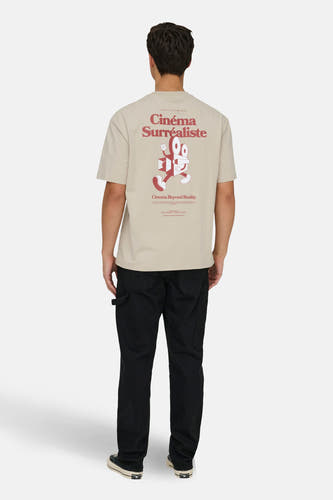 T-shirt écru à manches courtes de ONLY & SONS®, avec une impression 'Cinéma Surréaliste' sur le dos, porté avec un pantalon noir et des baskets.