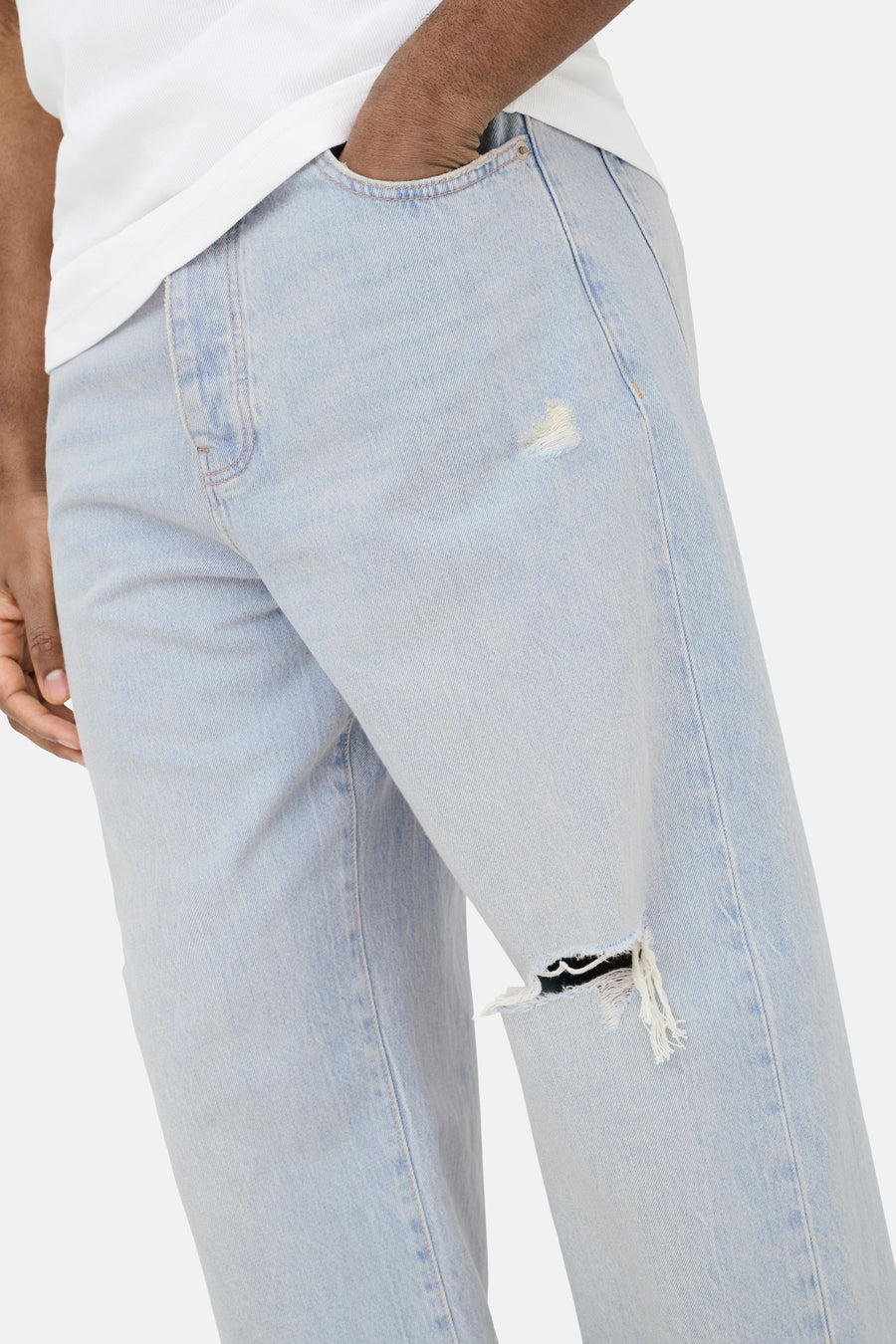 Jean large bleu clair en denim ONLY & SONS® avec déchirures, une main dans la poche et un t-shirt blanc.
